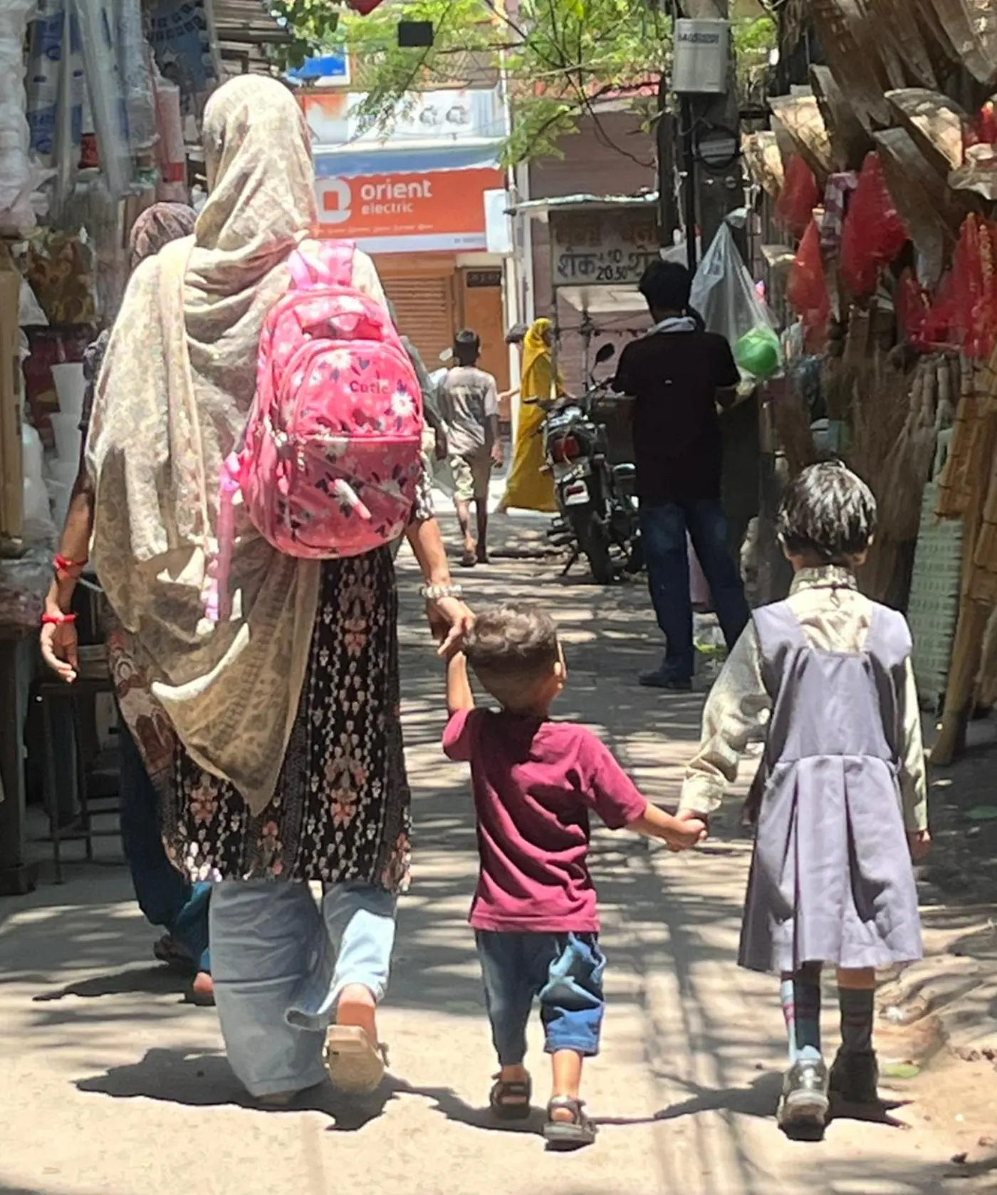 Mother walking her two young children through the market with a school backpack