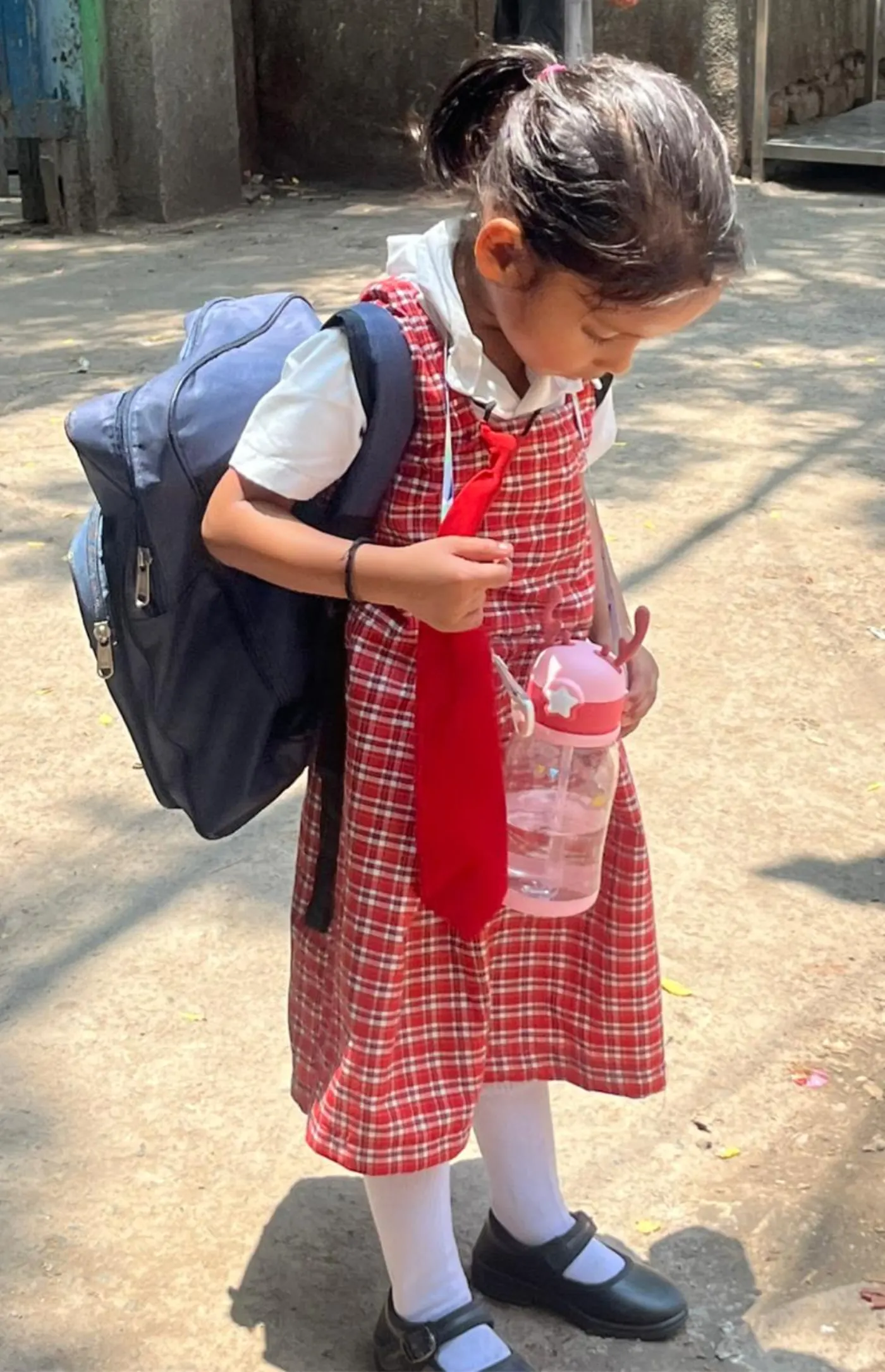 Little girl in school uniform carrying her backpack and water bottle